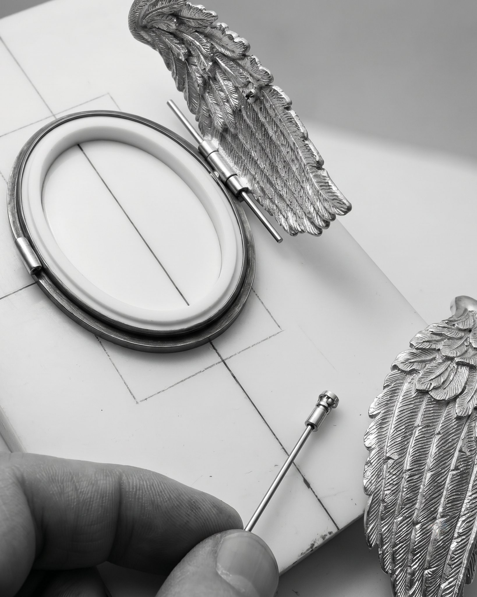 Close-up of a winged metal ornament with a small precision tool on a drafting surface.