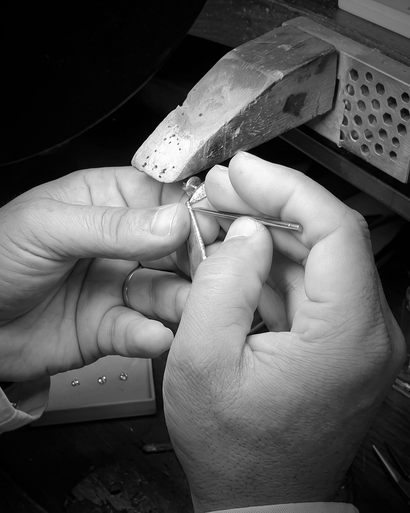 Close-up of hands using pliers to shape a small metal piece during jewelry making at a workbench.