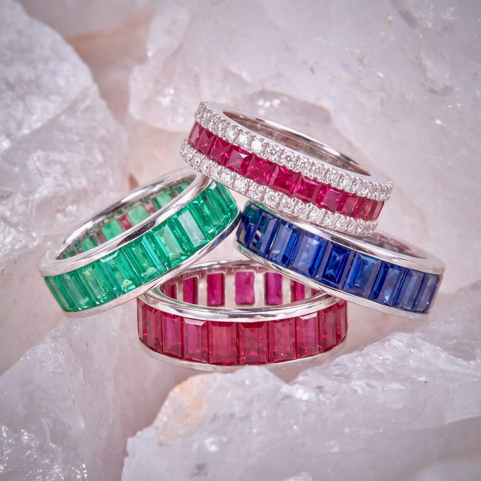 Stacked silver bangles set with rectangular green, pink, blue, and pink red gemstones surrounded by small diamonds, displayed on a crystalline background