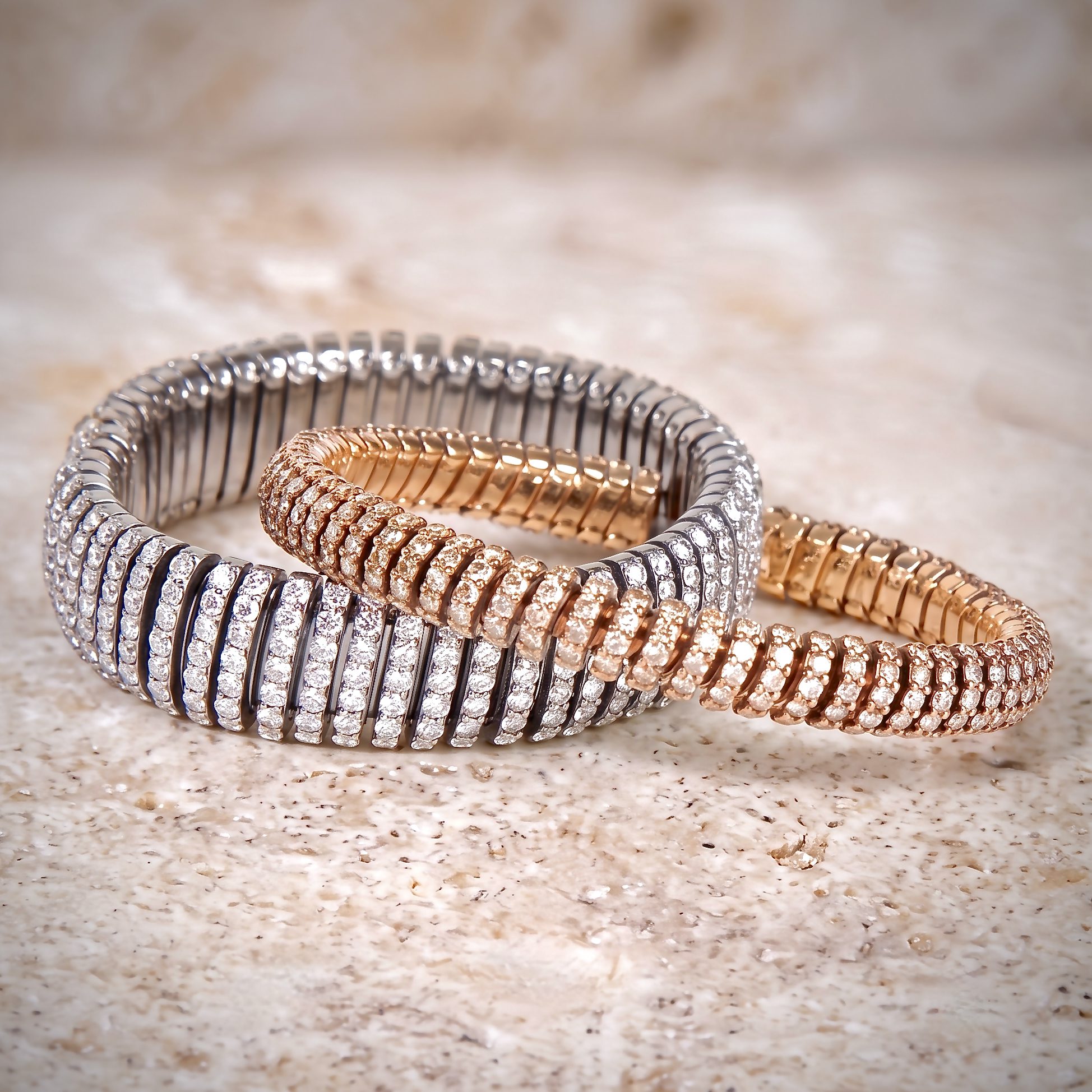 Coiled silver and rose-gold bracelets with rhinestones on a speckled beige countertop, close-up view of jewelry jumble on a surface.