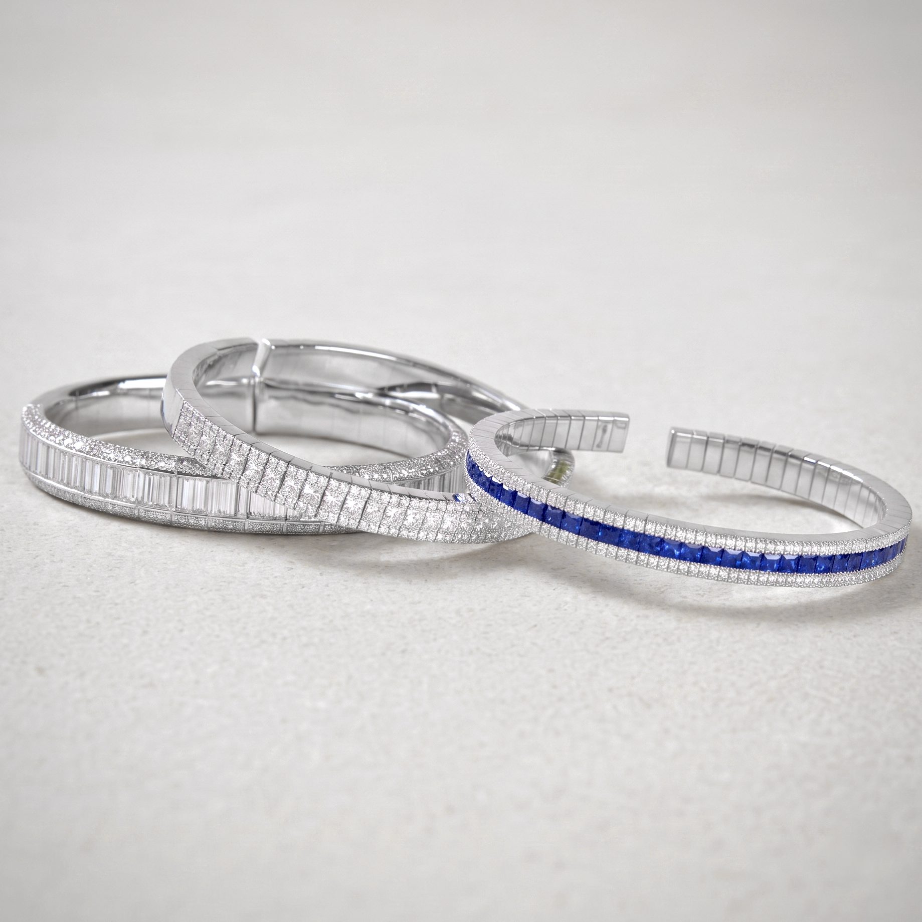 Close-up of silver diamond-studded bracelets coiled on a pale surface, showcasing sparkly links and a blue inlay variant.