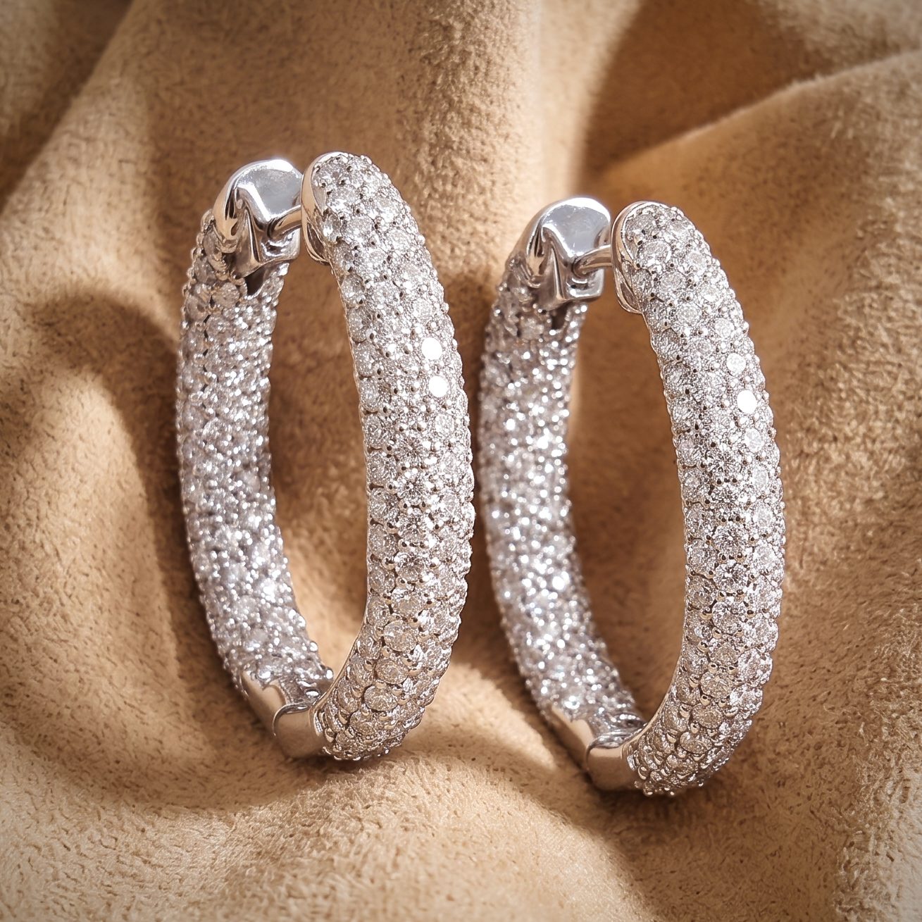 Two silver diamond-studded bracelets with textured pavé surfaces resting on tan fabric.