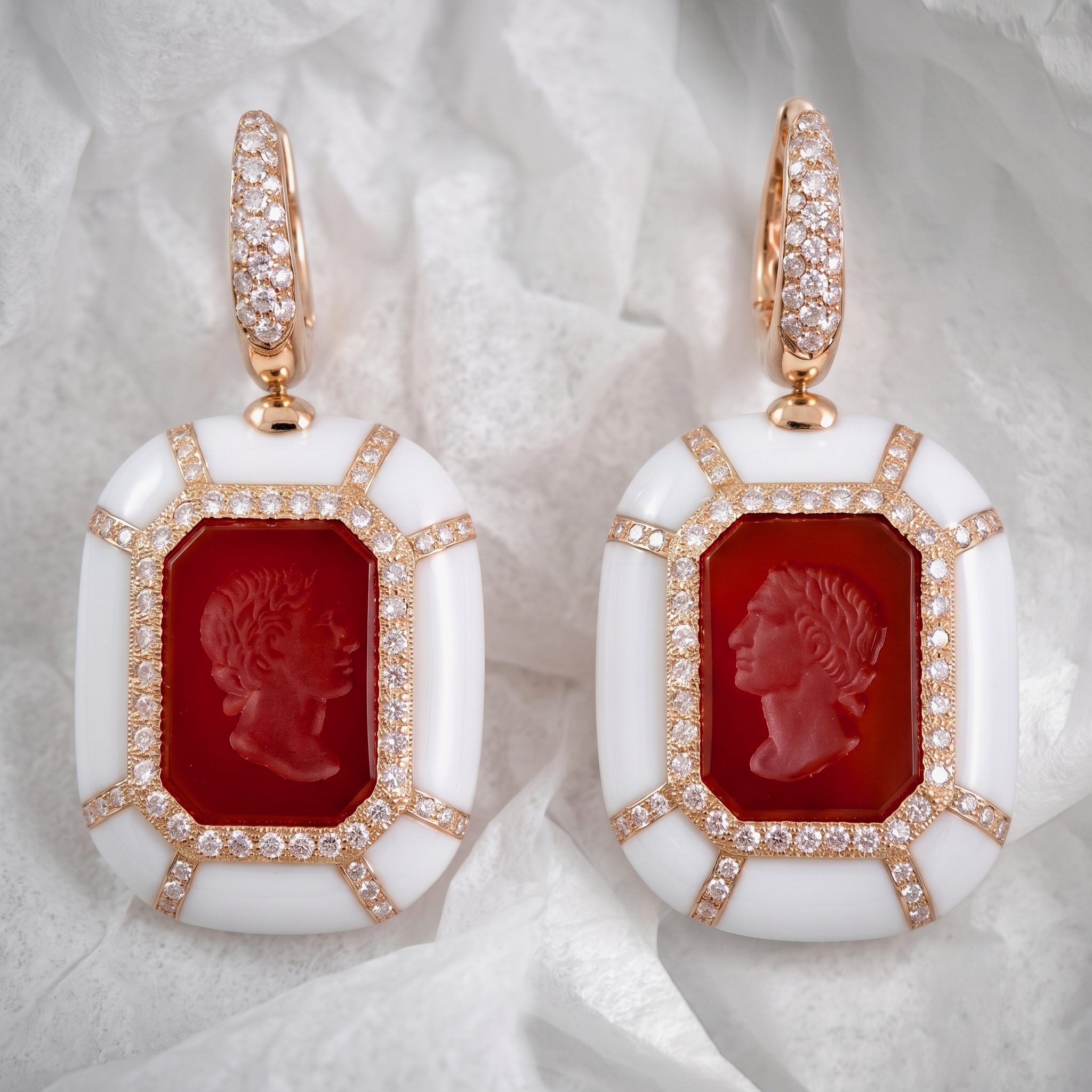 Two rose-gold earrings with pavé diamonds and a red octagonal centerpiece on pale fabric.