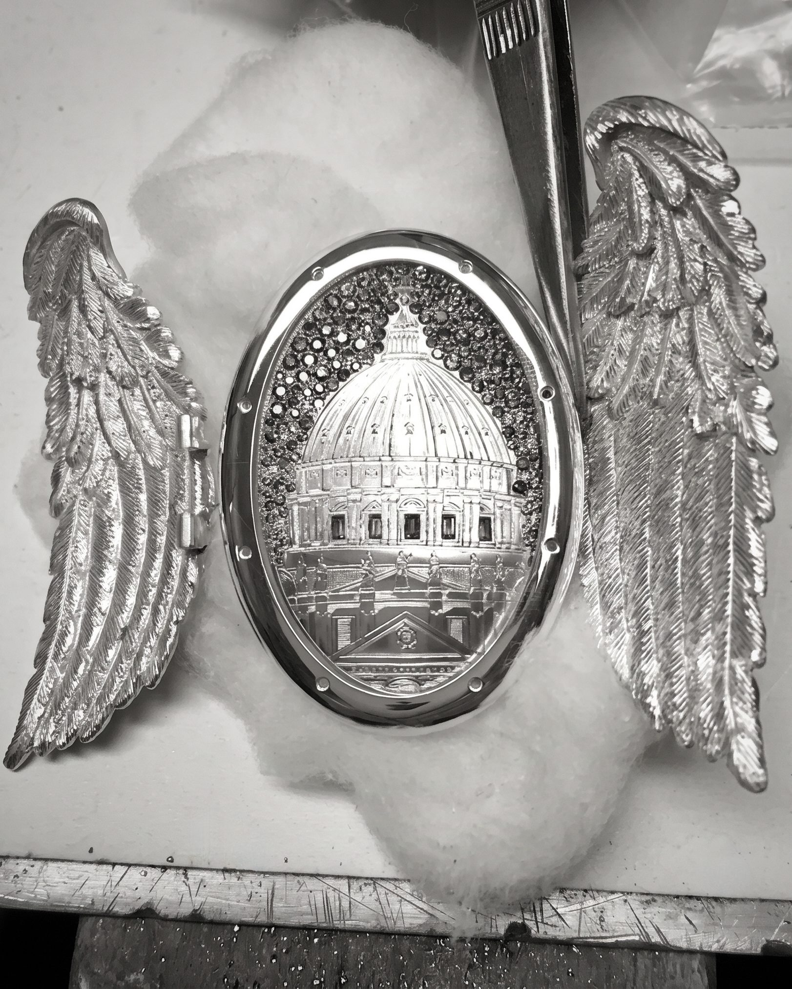 Close-up of a silver winged badge with a domed central design on a white surface.