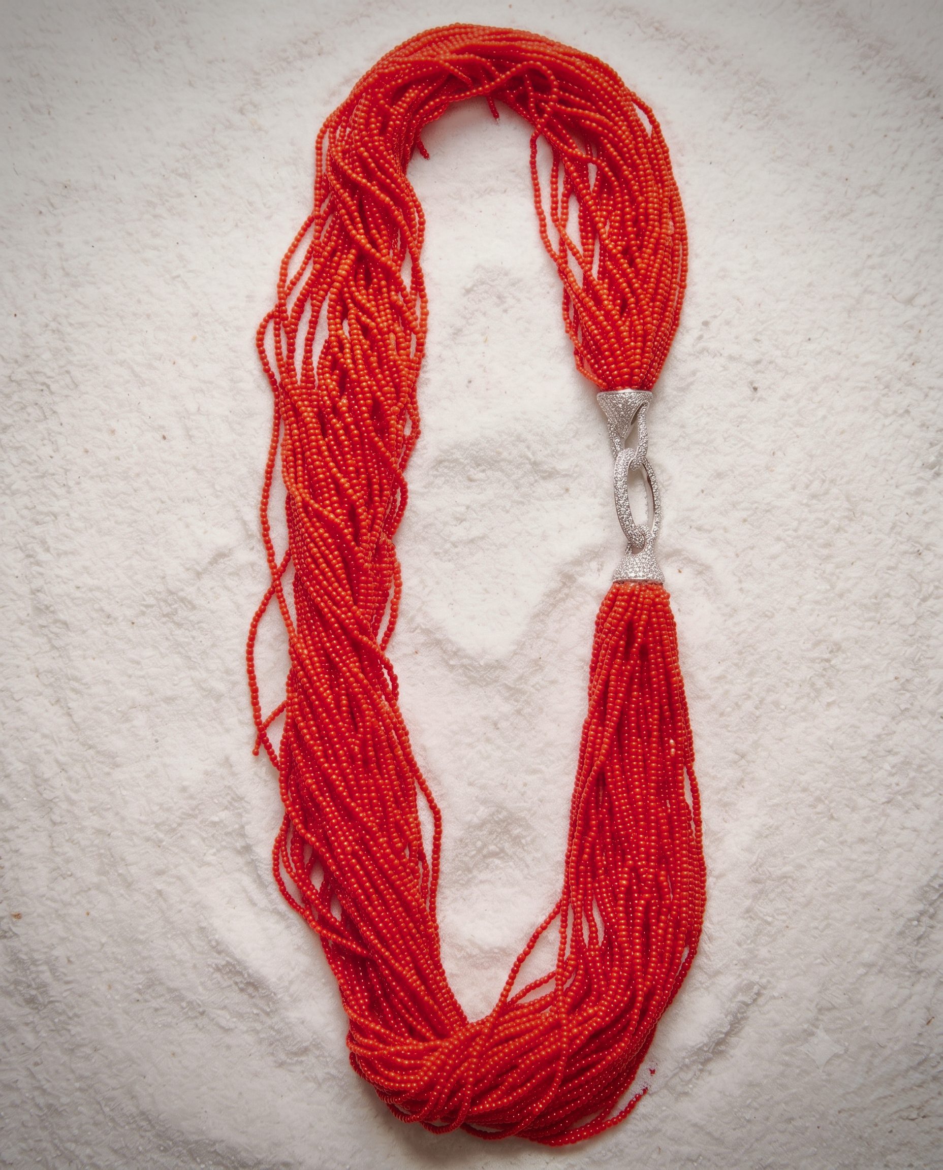 Long red beaded necklace with a silver clasp laid on a light textured surface