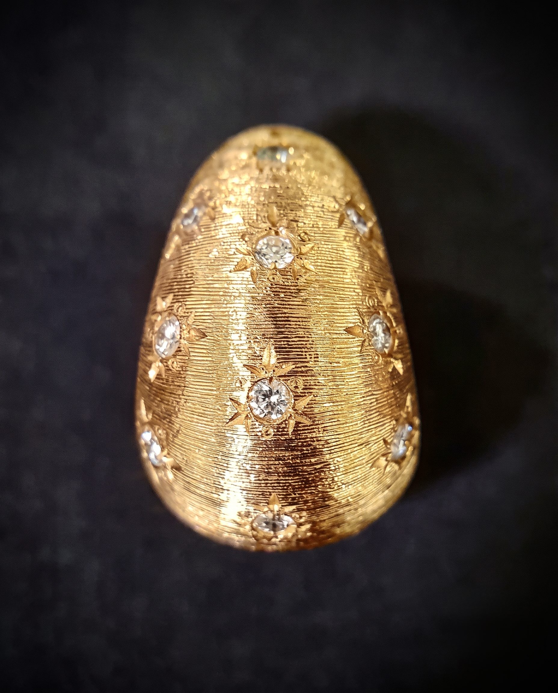 Ornate gold egg-shaped jewelry piece with diamond inlays and floral engravings on a dark background.