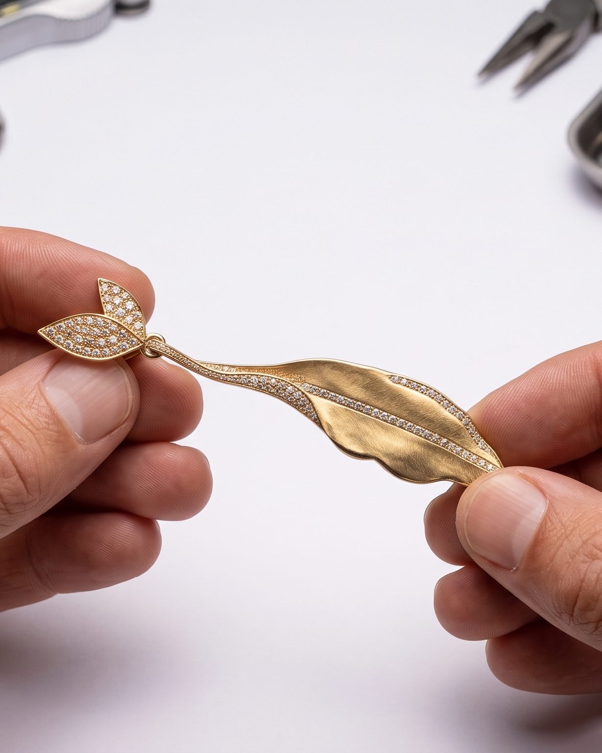Gold leaf pendant encrusted with small diamonds, held between two fingers against a white background.