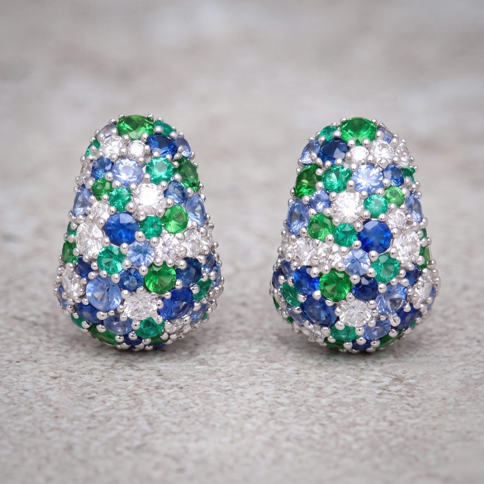 Two crystal-encrusted eggs in green, blue, and clear stones resting on a speckled gray surface.