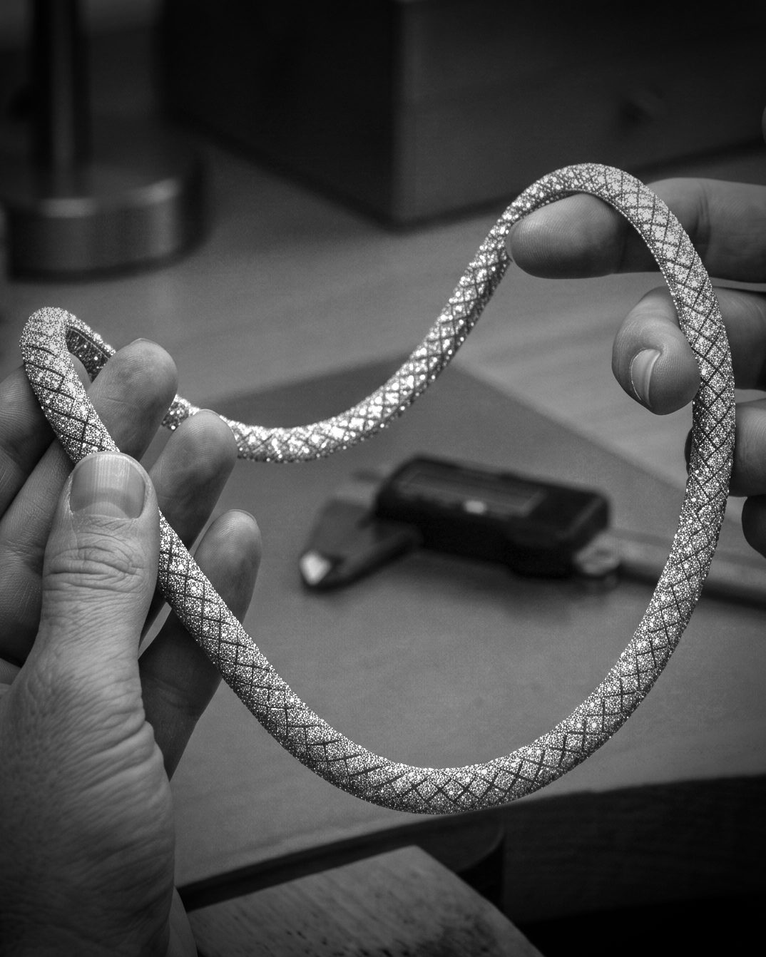 Two hands hold a sparkling diamond-patterned bracelet, showing its flexible lattice design.