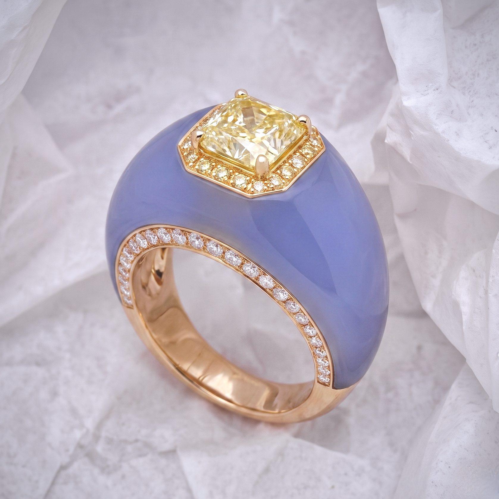 Gold ring with a square-cut yellow diamond centerpiece and a diamond-studded halo on a blue background.