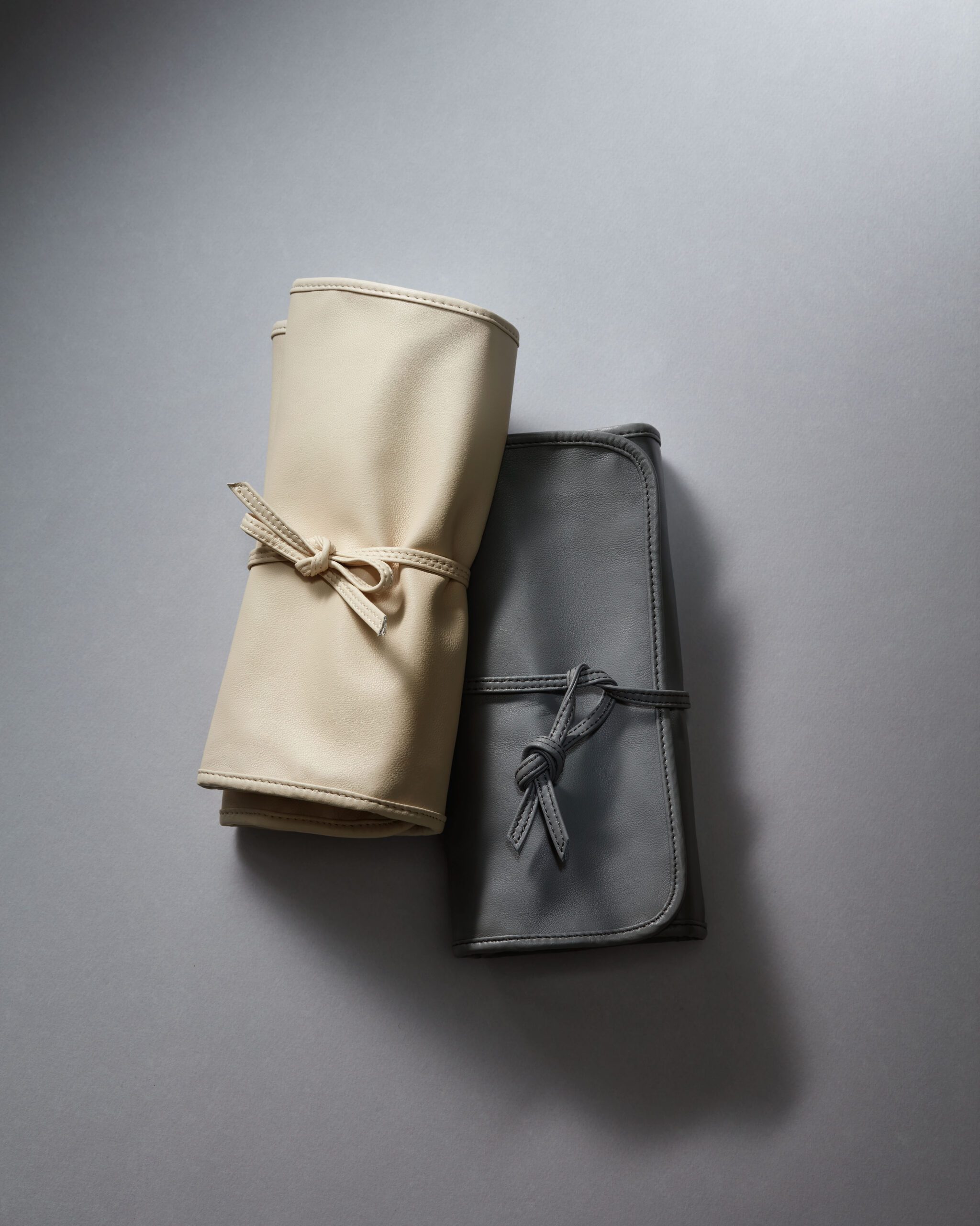 Beige rolled leather boot leaning against a gray handbag on a plain gray backdrop.