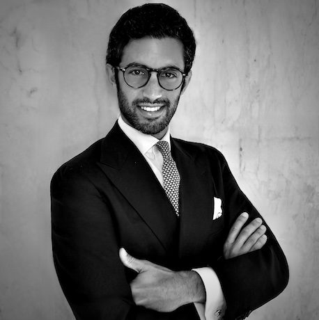 Professional man with glasses in a black suit, arms crossed, smiling at the camera.